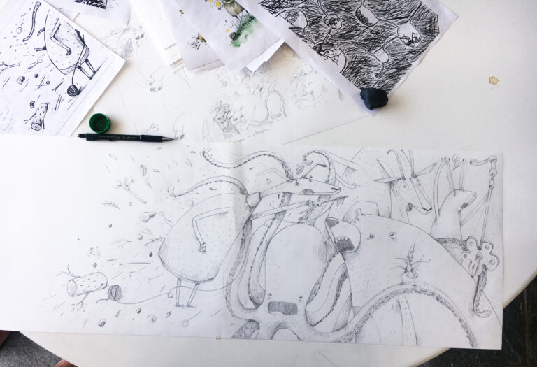 A pen and ink sketch of an octopus, bear, goat, rabbit, and reindeer is spread out on a white desk. There is a pen on the desk, as well as other preliminary sketches. 